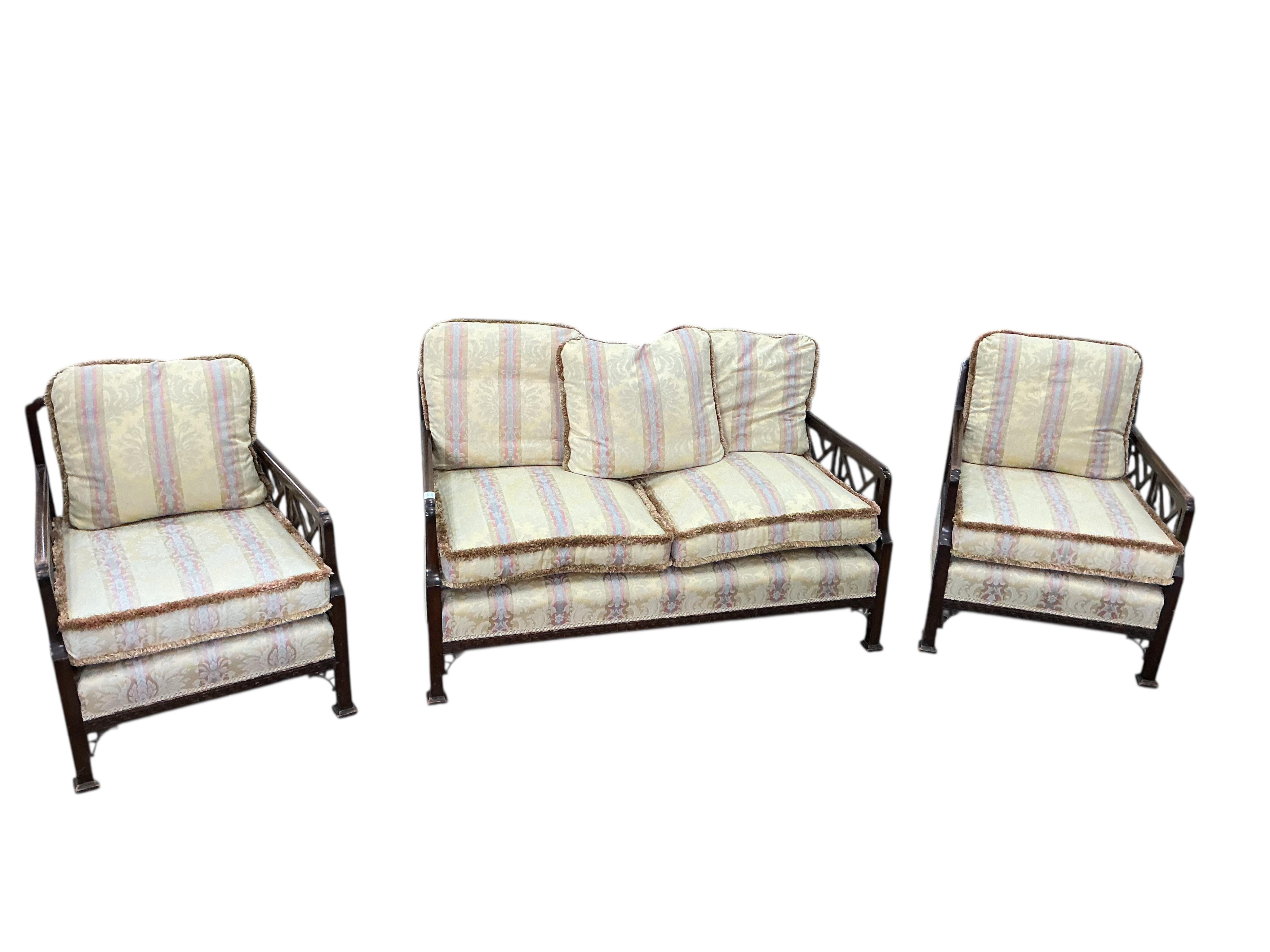 An early 20th century mahogany three piece suite comprising a sofa, width 134cm, depth 70cm, height 76cm and matching armchairs with fretwork sides